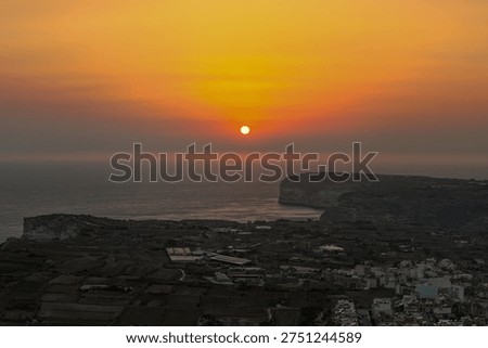 Sunset over Ta' Cenc Cliffs near Sannat, Gozo, with coastal plateau, farmland plots and village buildings above the Mediterranean Sea.