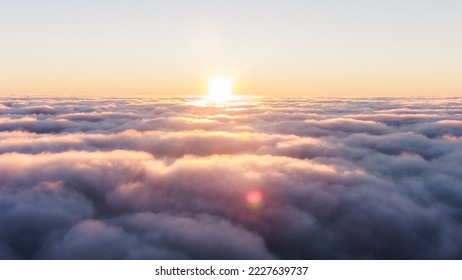 Sunset over waves of heavy thick fog. Dark clouds of fog. The sun shines over heavy purple hazy clouds at high altitude: evening sunset above the clouds.