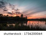 Sunset over Westport lake in Stoke on Trent, Staffordshire, UK.Tranquil evening landscape scene with colourful sky reflecting in water surface and silhouetted trees on horizon.