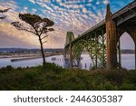 Sunset over Yaquina Bay Bridge in Newport, Oregon with cloudy sky. The Yaquina Bay Bridge is an elegant art deco structure arching over the picturesque bay.