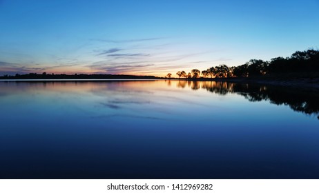 Sunset overlooking the lake, trees, clouds. The sky and bushes are reflected in the water. Landscape at dusk. Nightfall. Water like a mirror.