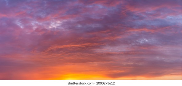 Sunset panorama of cloud blanket texture and detail brightly colorful lit up orange from below with blue tints in the background. Painterly vibrant weather condition wallpaper backdrop.