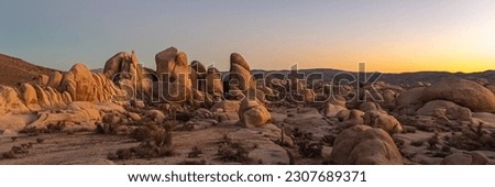 Sunset panoramic rock formations in Joshua Tree National Park during autumn with rock, desert panorama scenic landscape views with blue sky, clouds. Orange, purple, blue tones in sky.
