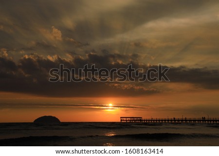 a sunset with the ray of light between an island and the jetty neayby the seaside
