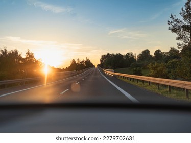 sunset rays shining through trees on open country road view from inside car
