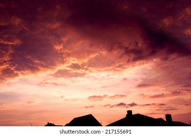 Sunset red sky with dark dramatic clouds over houses.