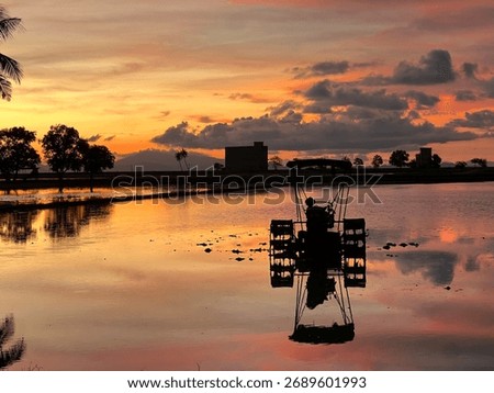 Sunset reflection with a paddy field tractor. The orange sky and calm water create a peaceful rural landscape, symbolizing traditional agriculture and countryside life in Perlis, Malaysia