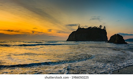Sunset at Ruby Beach. Huge stones in the water. The sun reflects in waves. Olympic National Park, Washington state, USA