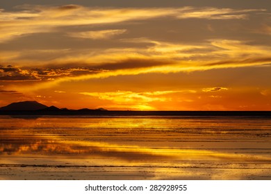 Sunset in Salar de Uyuni. Reflection of the sun in the wet surface of salt. Mountain background
