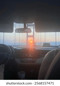 Sunset shining through windshield while driving over bridge