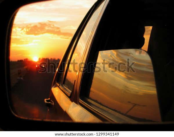 Sunset in\
the side mirror of a car during a road\
trip.