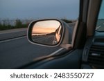 Sunset in the side mirror. View from the the drivers seat while driving the car in the evening.