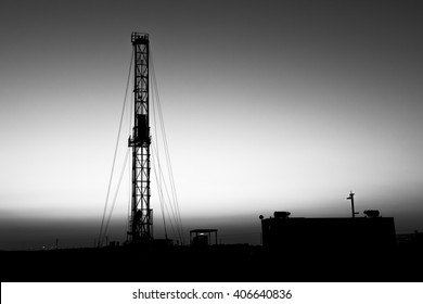 Sunset and silhouette of drilling rig in oilfield - black and white