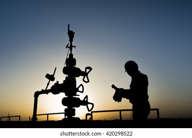 Sunset and silhouette of oilfield worker inspecting the wellhead in oilfield 