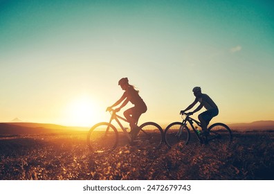 Sunset, silhouette and people on bicycle with adventure, race and exercise in nature together. Cycling, fitness and friends with mountain bike in evening for outdoor workout, blue sky and grass path - Powered by Shutterstock