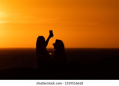 Sunset Silhouette: Same Sex Couple Of Girls At Sunset In Camps Bay Tidal Pool, Cape Town, South Africa