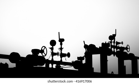 Sunset and silhouette of wellhead manifold controls in the oilfield - black and white
