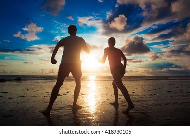 Sunset Silhouette Of Young Couple In Love Running At Beach