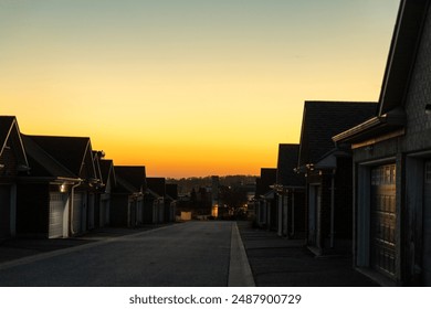 Sunset sky above suburban street - row of houses with prominent garages - warm golden hour light casting long shadows - clear, cloudless horizon - tranquil residential scene - Powered by Shutterstock