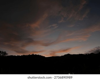 Sunset sky with dramatic clouds above dark hill silhouettes in the evening, creating a calm and emotional atmosphere in a natural landscape.