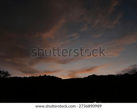 Sunset sky with dramatic clouds above dark hill silhouettes in the evening, creating a calm and emotional atmosphere in a natural landscape.