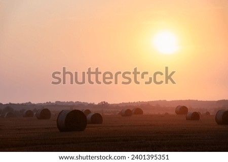 Sunset sky glowing on round bales of dry hay on an agricultural field. Rural landscape with straw rolls and dramatic sunrise sky