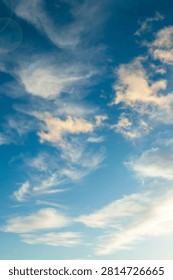 Sunset sky landscape, vertical view of a vibrant blue sky populated by scattered, wispy cirrus and light cumulus clouds lit by soft sunlight