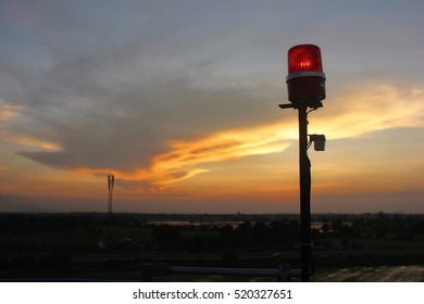 Sunset sky with red warning light silhouette on building rooftop.