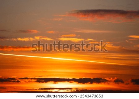 Sunset sky with some clouds and an airplane trail. Red orange sunset with clouds