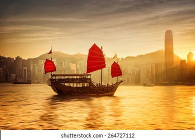 Sunset Skyline Of Hong Kong With Traditional Cruise Sailboat At Victoria Harbor