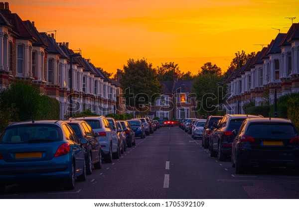 Sunset at a street of\
terraced houses with cars parked in resident bay around West\
Hampstead in London