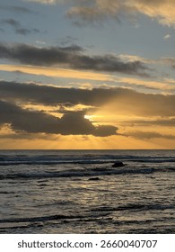 Sunset with the sun behind the clouds and the rays of the sun radiating through.The sea is calm with just a small waved 