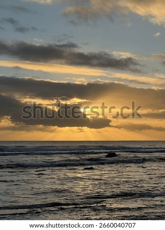 Sunset with the sun behind the clouds and the rays of the sun radiating through.The sea is calm with just a small waved 