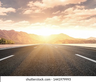 At Sunset, The Sun Shines On A Tarmac Road Stretching From The Lake To The Distant Mountains, Joining The Mountains.