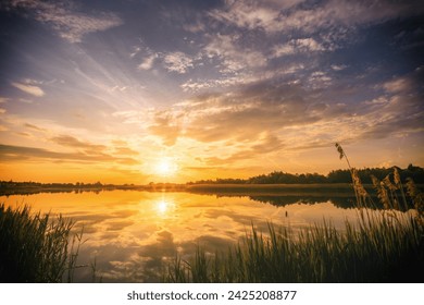 Sunset or sunrise above the pond or lake at spring or early summer evening or morning with cloudy sky background and reed grass. Springtime landscape. Water reflection. Vintage film aesthetic. - Powered by Shutterstock