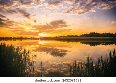 Sunset or sunrise above the pond or lake at spring or early summer evening or morning with cloudy sky background and reed grass. Springtime landscape. Water reflection. Vintage film aesthetic. - Powered by Shutterstock