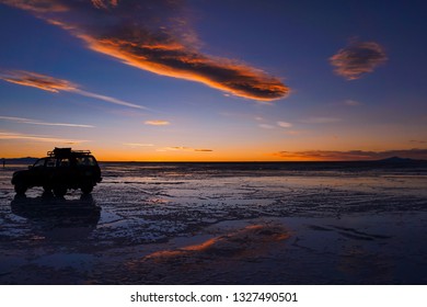 Sunset sunrise with car 4x4 jeep on the salar salt desert of de uyuni in bolivia with clouds and colors orange yellow pink deep blue on an adventure backpacking travel wanderlust enjoy nature