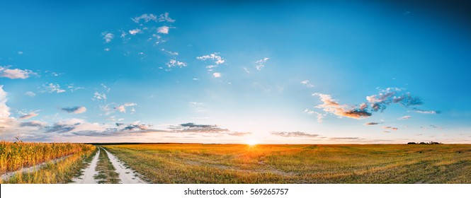 Sunset, Sunrise Over Rural Meadow Field And Country Open Road. Countryside Landscape With Path Way Under Scenic Summer Dramatic Sky In Sunset Dawn Sunrise. Sun Over Skyline Or Horizon.