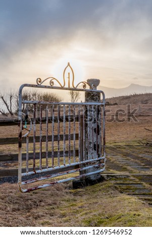 Sunset through the cross in the rusted metal gate for the historic Kalfafellsstadur Church in Iceland