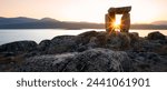 Sunset through Inuksuk in rough arctic landscape. Sunstar on the horizon in the fjord of Qikiqtarjuaq, Broughton Island, Nunavut.