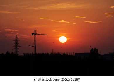 Sunset in Timisoara, Romania with cran cranes and electricity pylons with the sun and a bright red and orange sky - Powered by Shutterstock