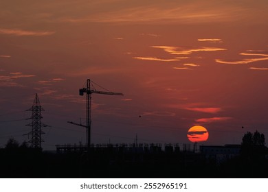 Sunset in Timisoara, Romania with cran cranes and electricity pylons with the sun and a bright red and orange sky - Powered by Shutterstock