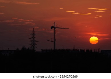 Sunset in Timisoara, Romania with cran cranes and electricity pylons with the sun and a bright red and orange sky - Powered by Shutterstock