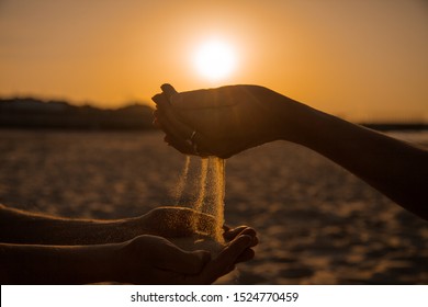 At sunset, two young people pour Golden sand from hand to hand, showing warm feelings. A symbol of eternal love and transience of life time on Earth. - Powered by Shutterstock