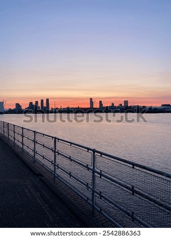 Sunset view along the Thames River in London, UK, with a pebbled shore in the foreground and the city skyline in the distance. A calm and scenic riverside landscape showcasing urban and natural beauty