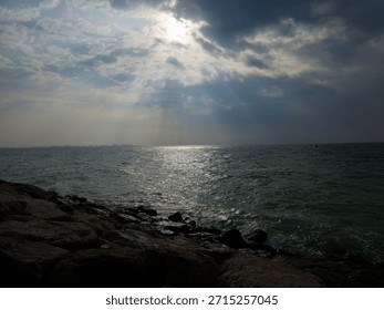 Sunset view from cloudy sky over the Sea with Rocks at beach. A beautiful sunset over the ocean with a large rock in the foreground. The sky is a mix of orange and pink hues, and the water is calm