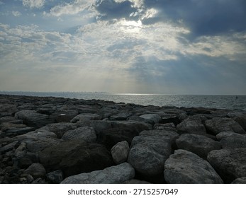 Sunset view from cloudy sky over the Sea with Rocks at beach. A beautiful sunset over the ocean with a large rock in the foreground. The sky is a mix of orange and pink hues, and the water is calm