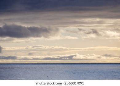 Sunset view of dramatic cloud formations over a calm sea horizon, providing a tranquil and serene ambiance. The natural composition evokes the beauty and peace of coastal scenery.