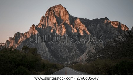 Sunset view of dramatic limestone mountains in La Huasteca Canyon, Monterrey, Mexico, with an empty road leading toward the rugged peaks under a clear sky.