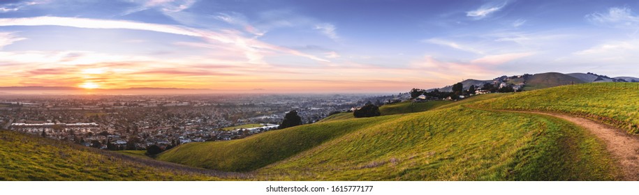 Sunset view of hiking trail on the verdant hills of East San Francisco Bay Area; the city of Hayward and the bay visible in the valley; California